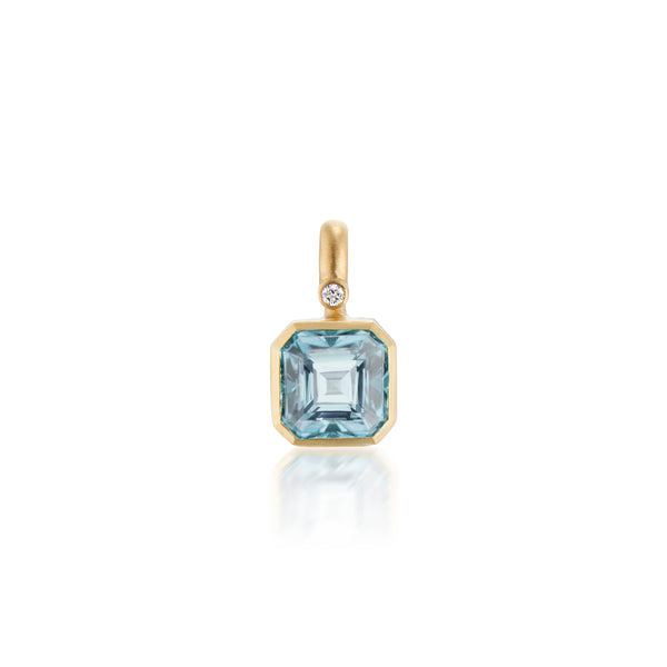 A gold pendant featuring a square-cut blue aquamarine gemstone and a small round diamond accent, shown on a clean white background with a soft reflection below.