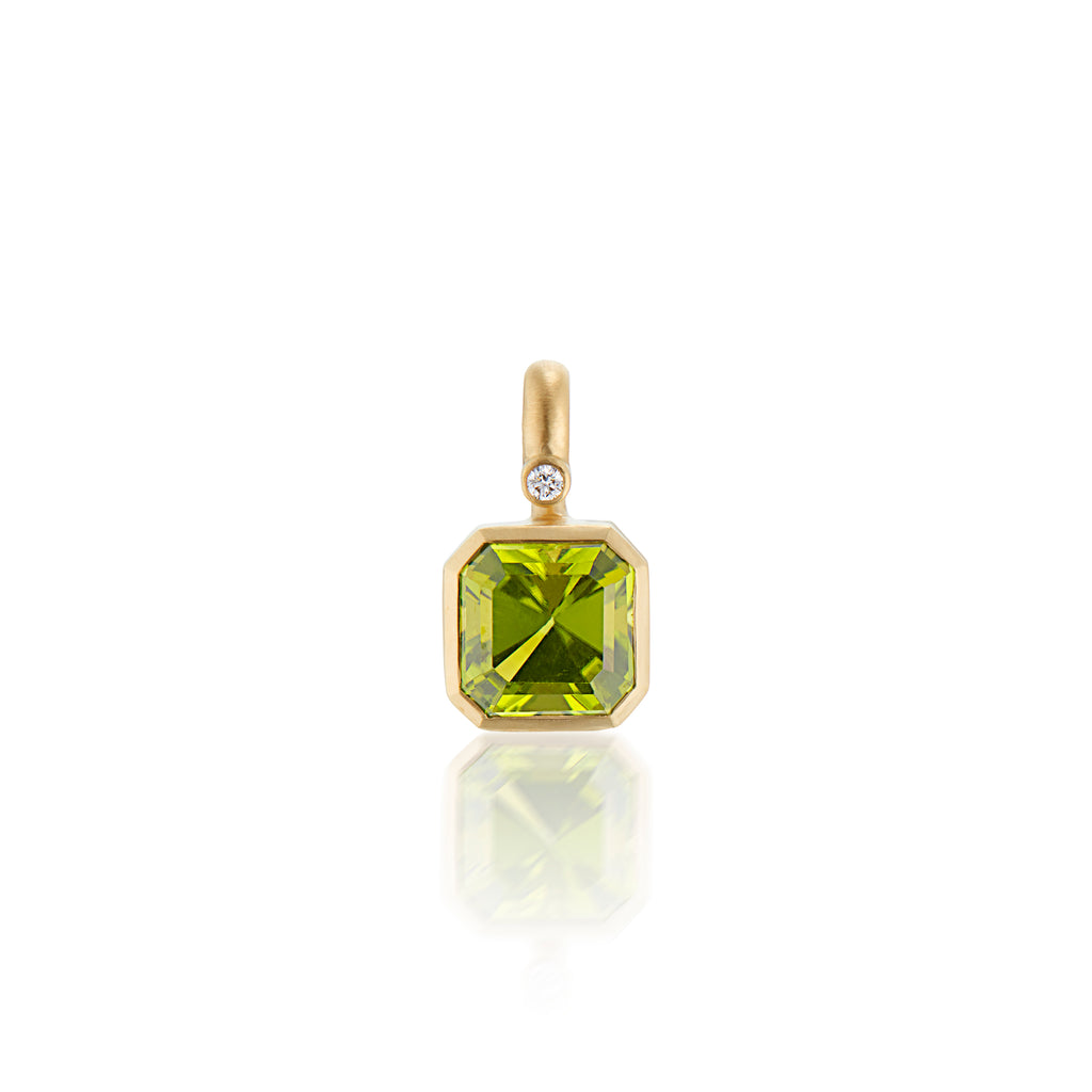 A gold pendant featuring a square-cut green peridot gemstone and a small round diamond accent, shown on a clean white background with a soft reflection below.