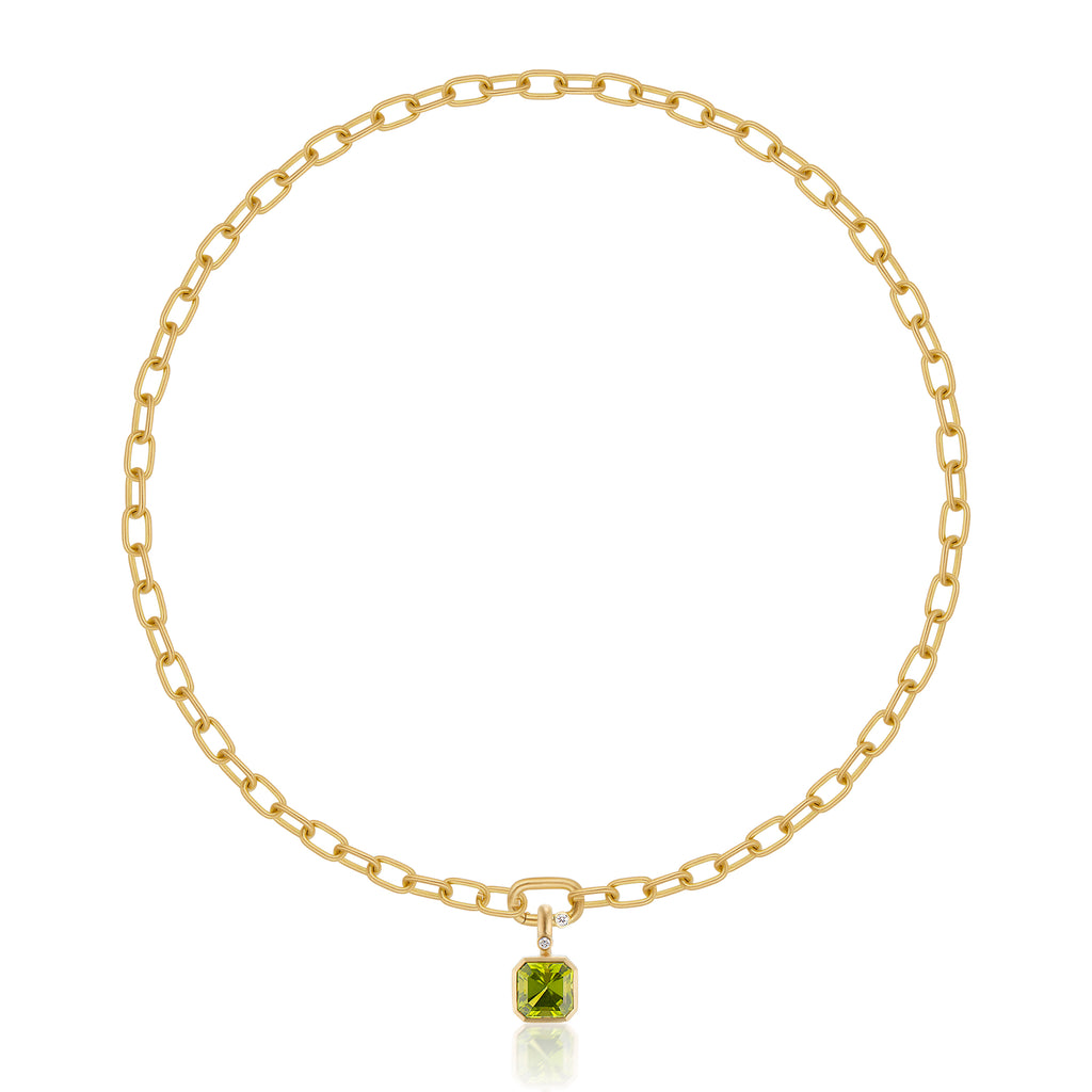 A gold chain necklace with a gold pendant featuring a square-cut green peridot gemstone and a small round diamond accent, shown on a clean white background with a soft reflection below.