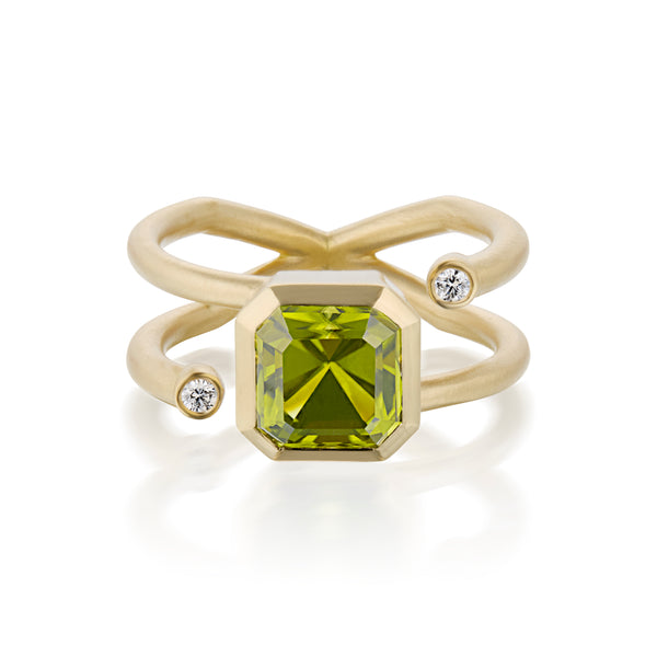 A gold ring featuring a large, faceted emerald-cut olive green Peridot or blue aquamarine center stone, with two wraparound gold bands adorned with small round-cut diamonds on either side, set against a clean white background.