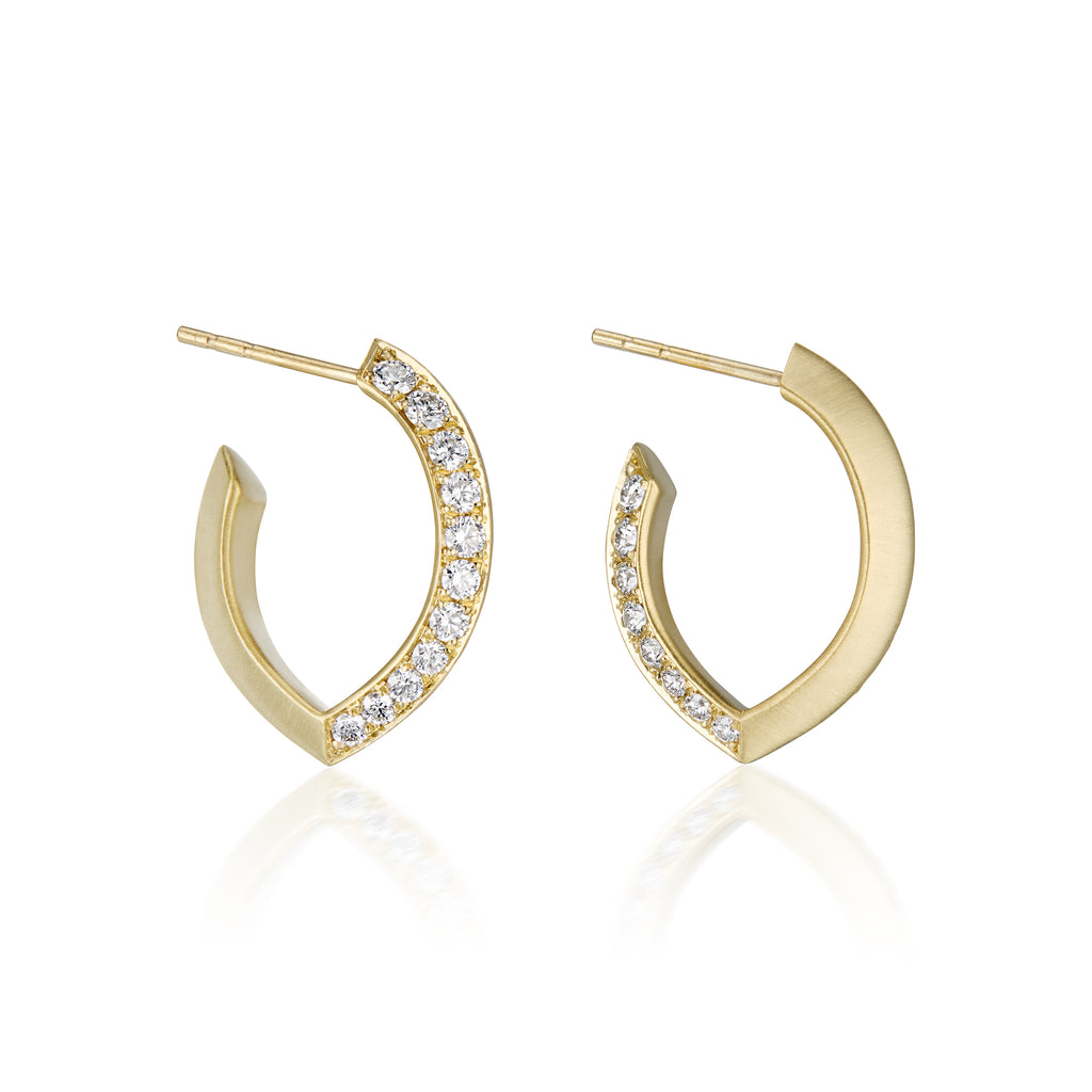 A pair of gold huggie hoop earrings with a row of diamonds pavé-set stones along the front edge, shown on a clean white background with a soft reflection below.