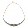 A curved collar necklace featuring a matte gray horn-like center pendant with a central gold gemstone, grossular garnet, suspended from a delicate gold chain against a white background.