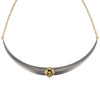 A curved collar necklace featuring a matte gray horn-like center pendant with a central gold gemstone, grossular garnet, suspended from a delicate gold chain against a white background.